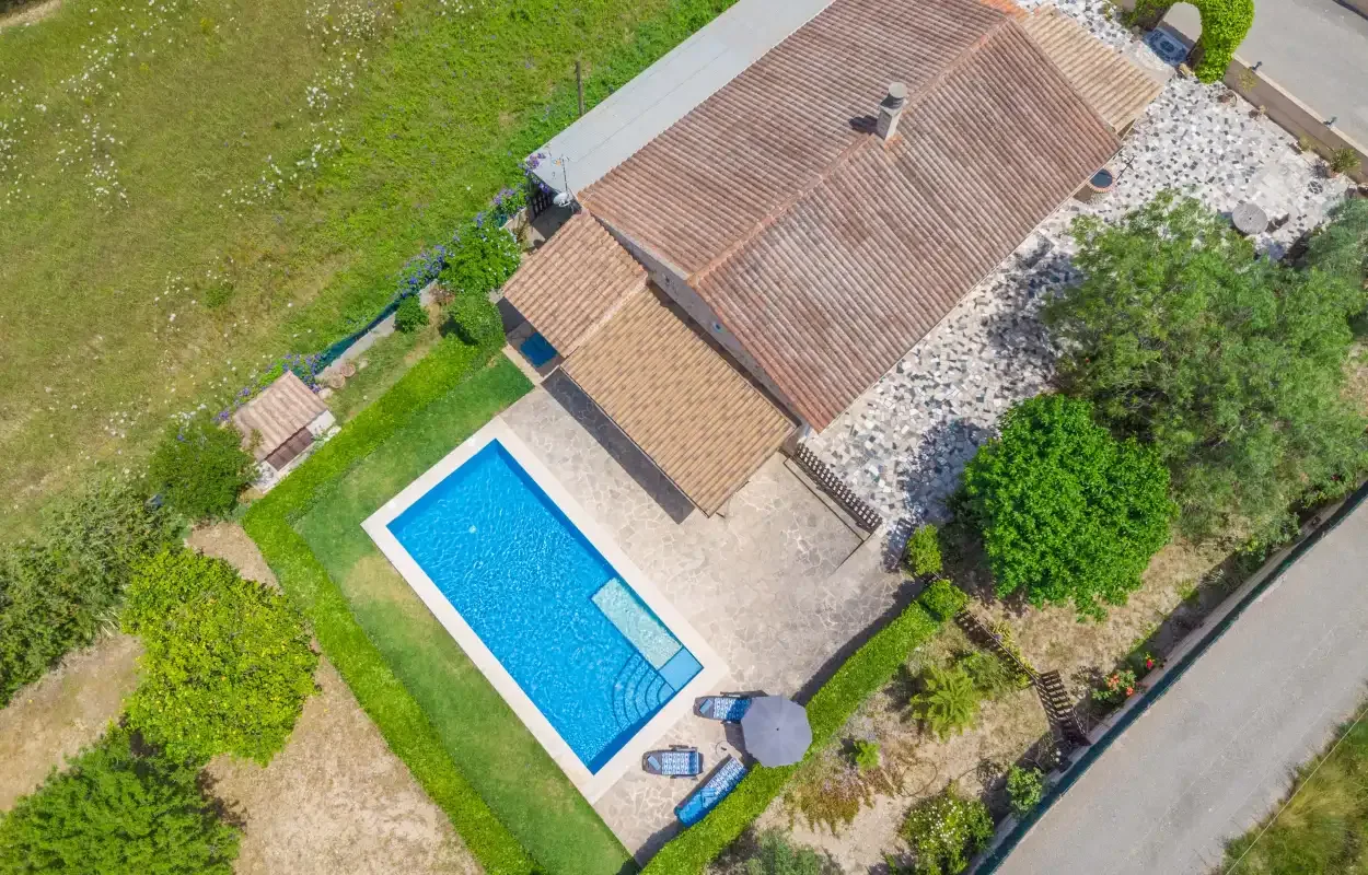 An aerial view shows a house beside a swimming pool and surrounding greenery.