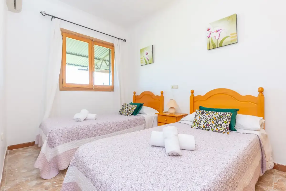 A bedroom with two beds, orange wooden headboards, and a window.