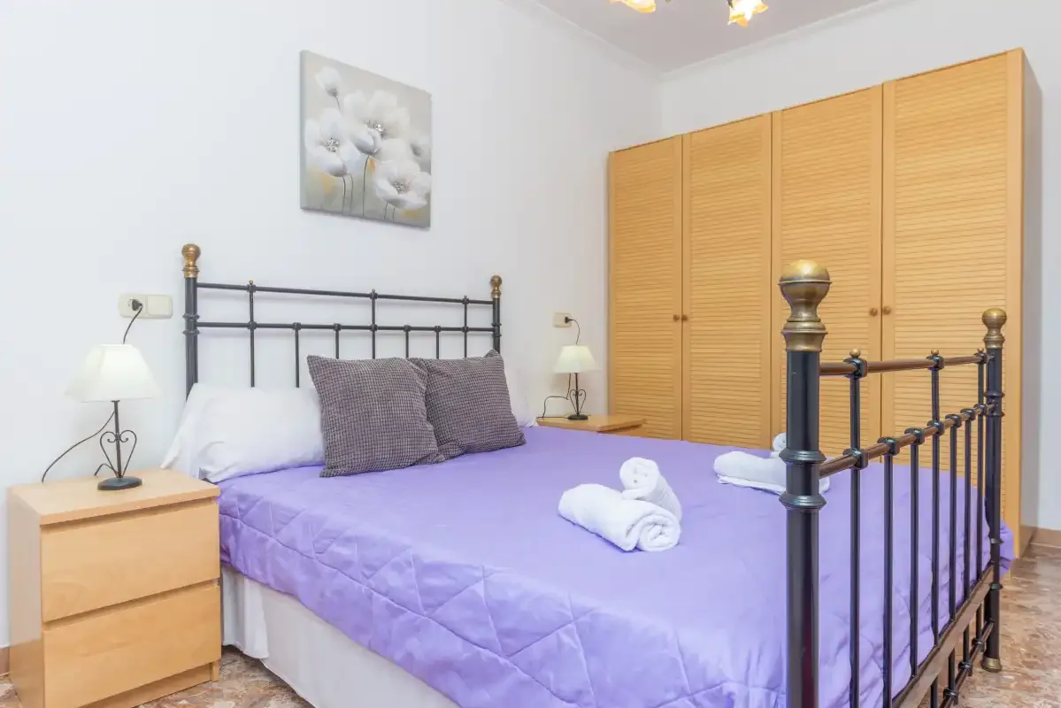 A bedroom with a purple bedspread and wooden wardrobes.