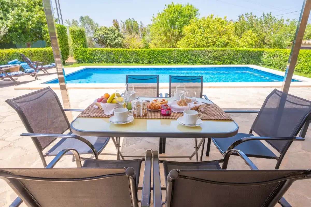 A patio dining area overlooks a swimming pool and greenery.
