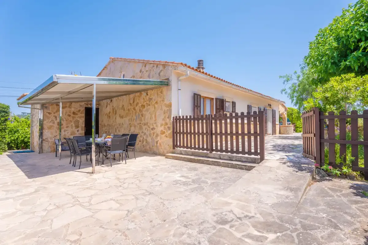 A stone patio beside a house has outdoor seating under a canopy and a wooden gate.