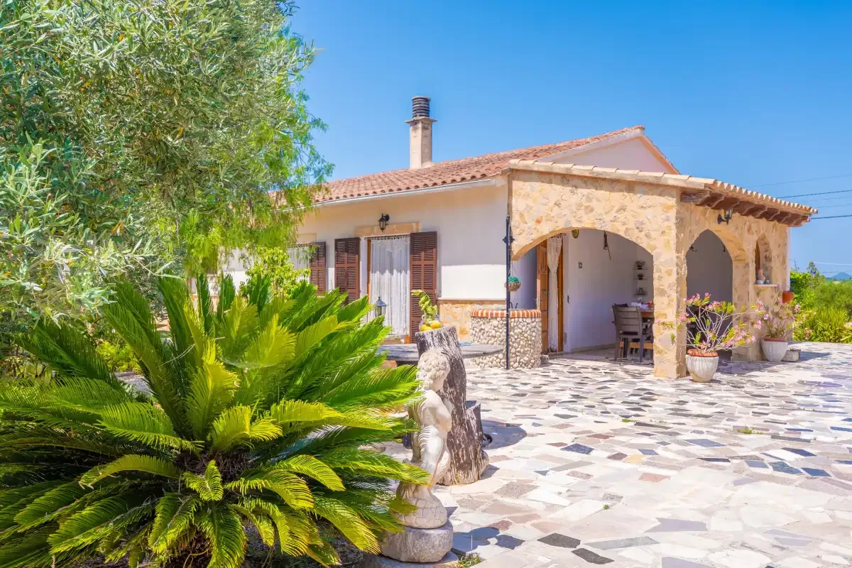 A tiled patio beside a house with a stone arched porch and leafy plants.