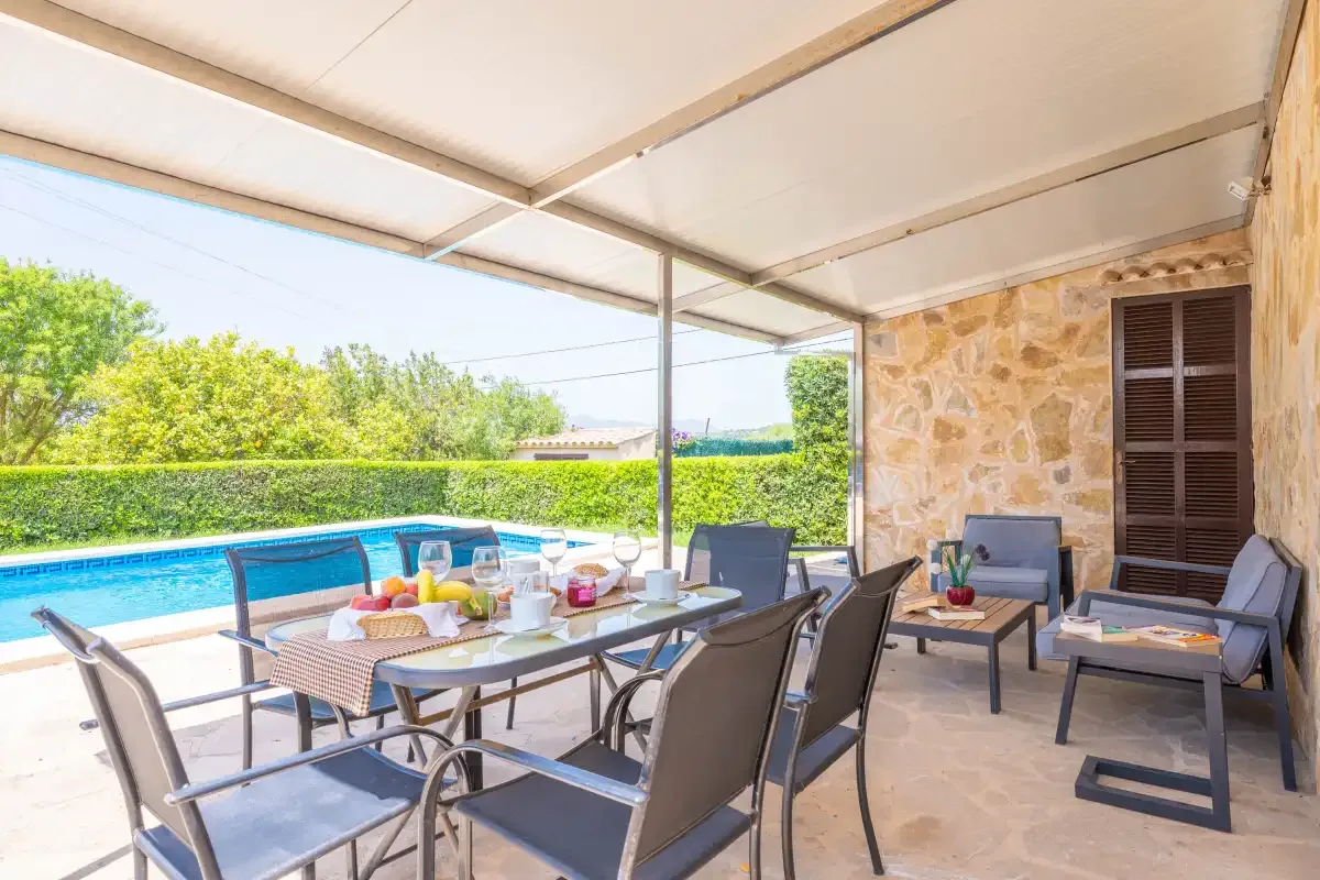 A covered outdoor dining and seating area beside a swimming pool.