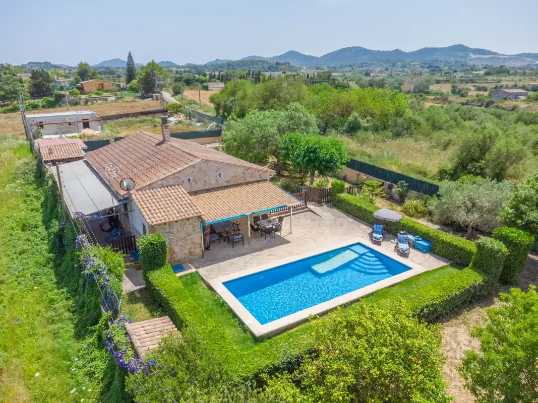 A countryside house and swimming pool are surrounded by greenery and open fields.