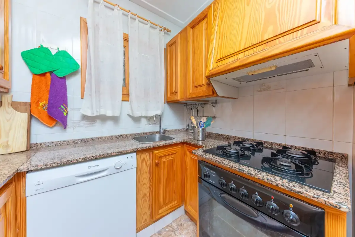 A kitchen with wooden cabinets, a sink, and a stovetop.