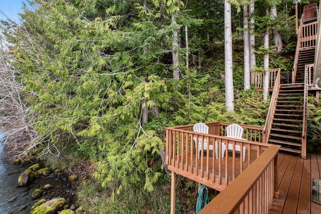 A wooden deck with seating overlooks a rocky stream among trees.