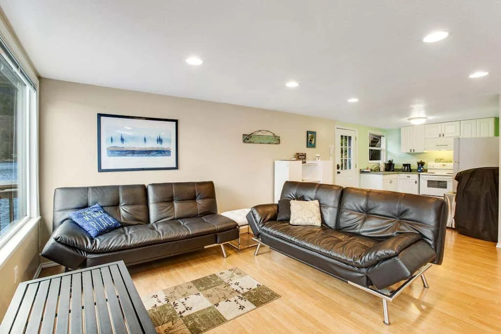 A living room with leather seating, a coffee table, and an open kitchen in the background.