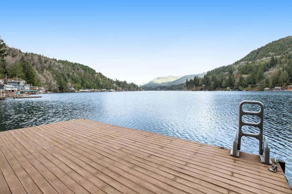 A wooden dock extends over a lake surrounded by wooded hills.