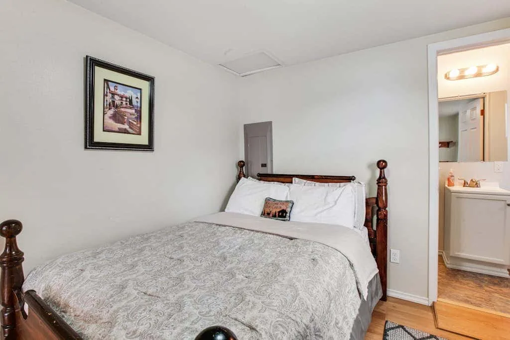 A bedroom with a bed dressed in white bedding and a gray cover.