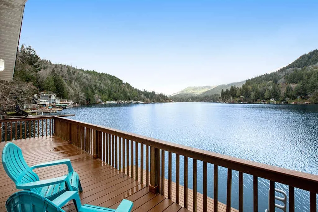 A wooden deck overlooks a lake, with turquoise seating beside the railing.
