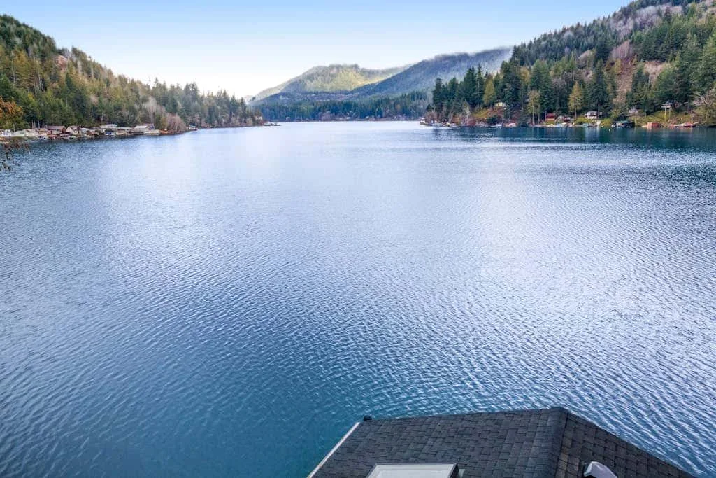 A lake stretches between forested hills, with a roof visible in the foreground.