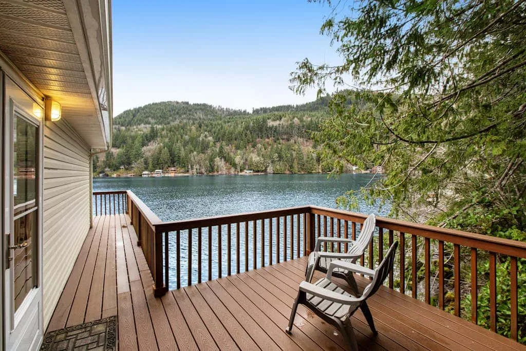 A wooden deck overlooks a lake, with seating beside the railing.