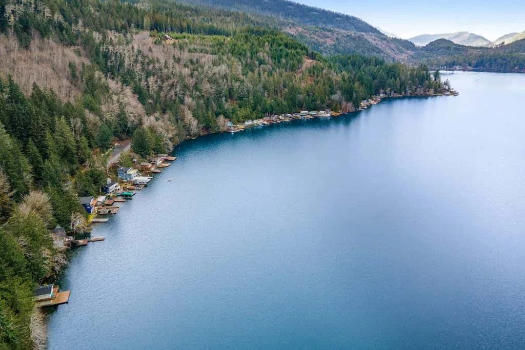 A lakeside shoreline curves beneath forested hills, with small docks along the water.