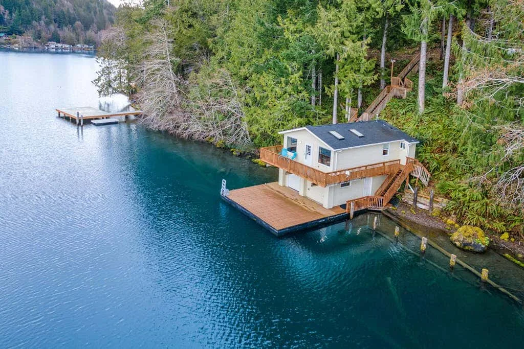 A lakeside house stands among trees beside a wooden dock.