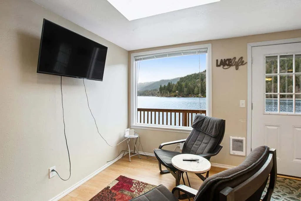 A sitting area with chairs faces a large window overlooking a lake and wooded hills.
