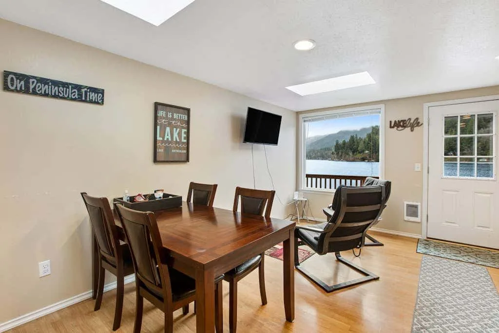 A dining and sitting area with a wooden table, chairs, and a lakeside view.
