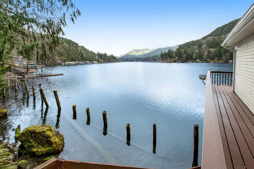 A lakeside deck overlooks calm water, with wooded hills along the shore.