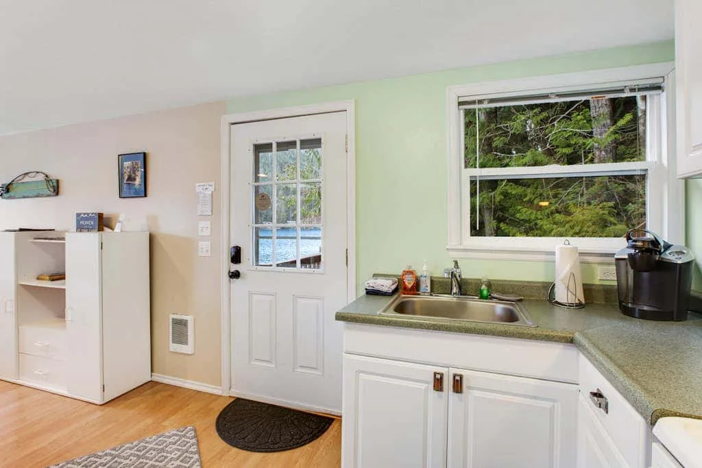 A compact kitchen with a sink beneath a wide window and a glass-paneled door.