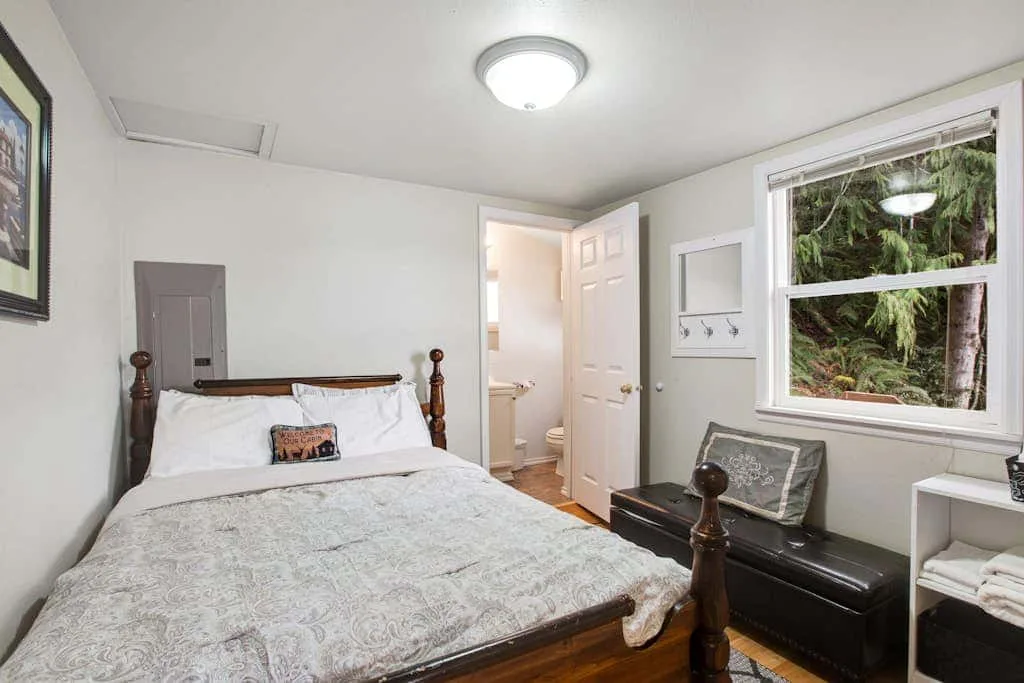 A bedroom with a wooden bed, white bedding, and a window overlooking greenery.