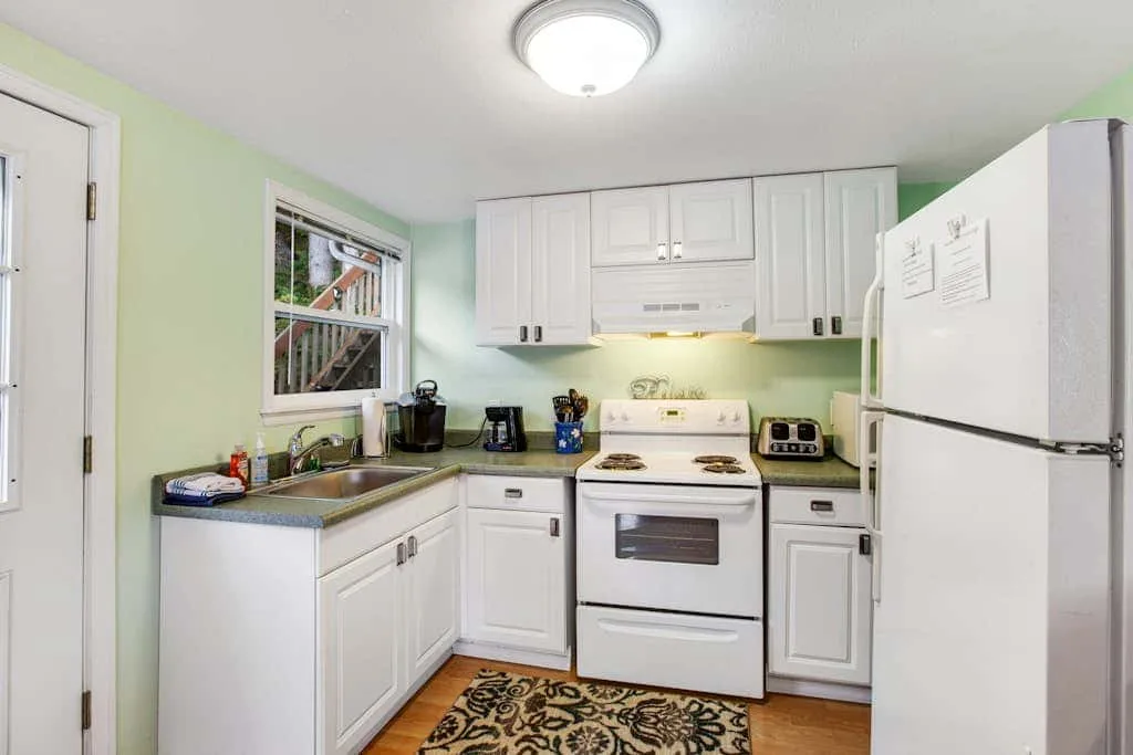 A bright kitchen with white cabinets, a stove, and a refrigerator.