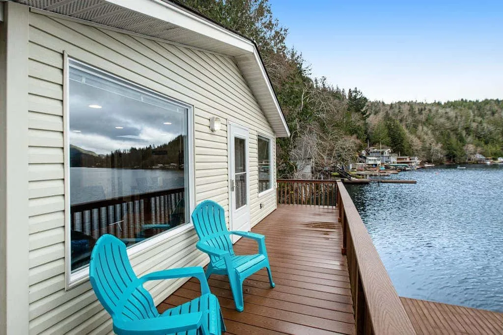 A wooden deck beside a lakeside building has two bright blue chairs.