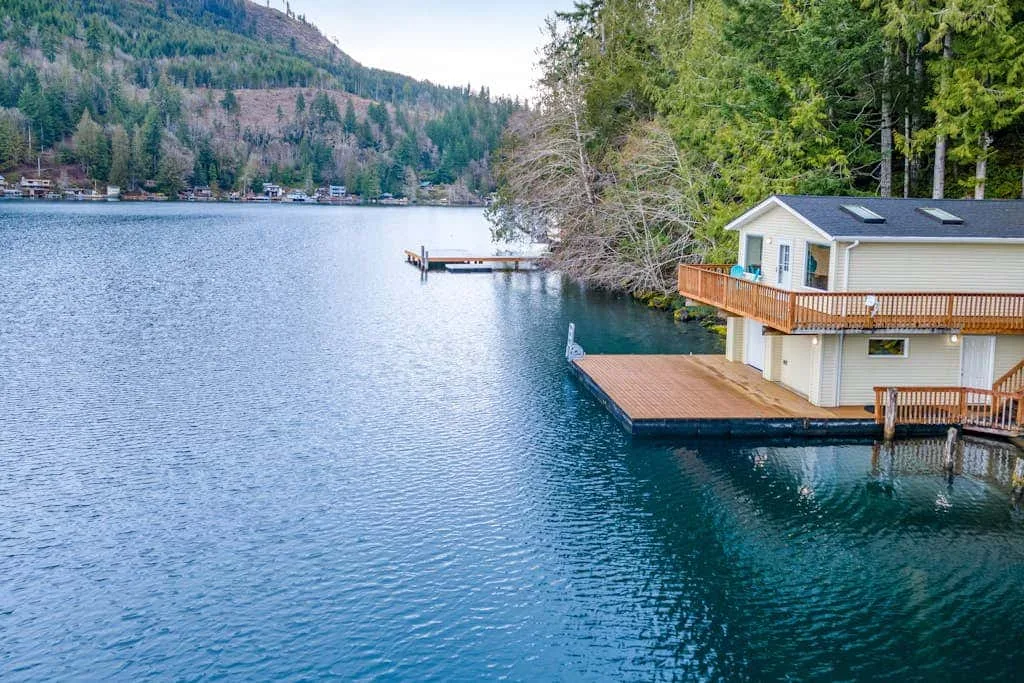 A lakeside building with wooden decks extends over the water beside a forested shore.