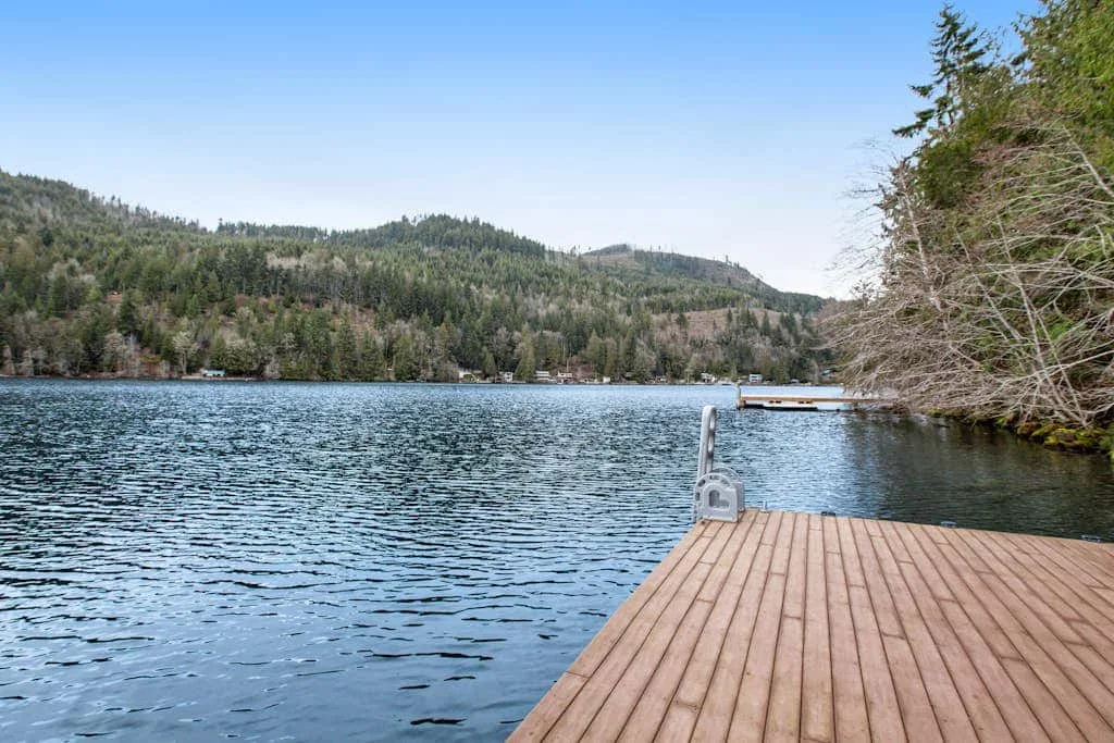 A wooden dock extends over a lake, with forested hills across the water.