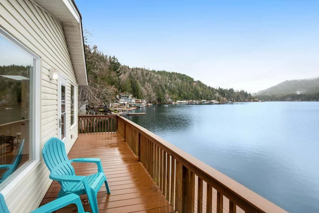 A wooden lakeside deck with turquoise seating overlooks calm water and wooded hills.