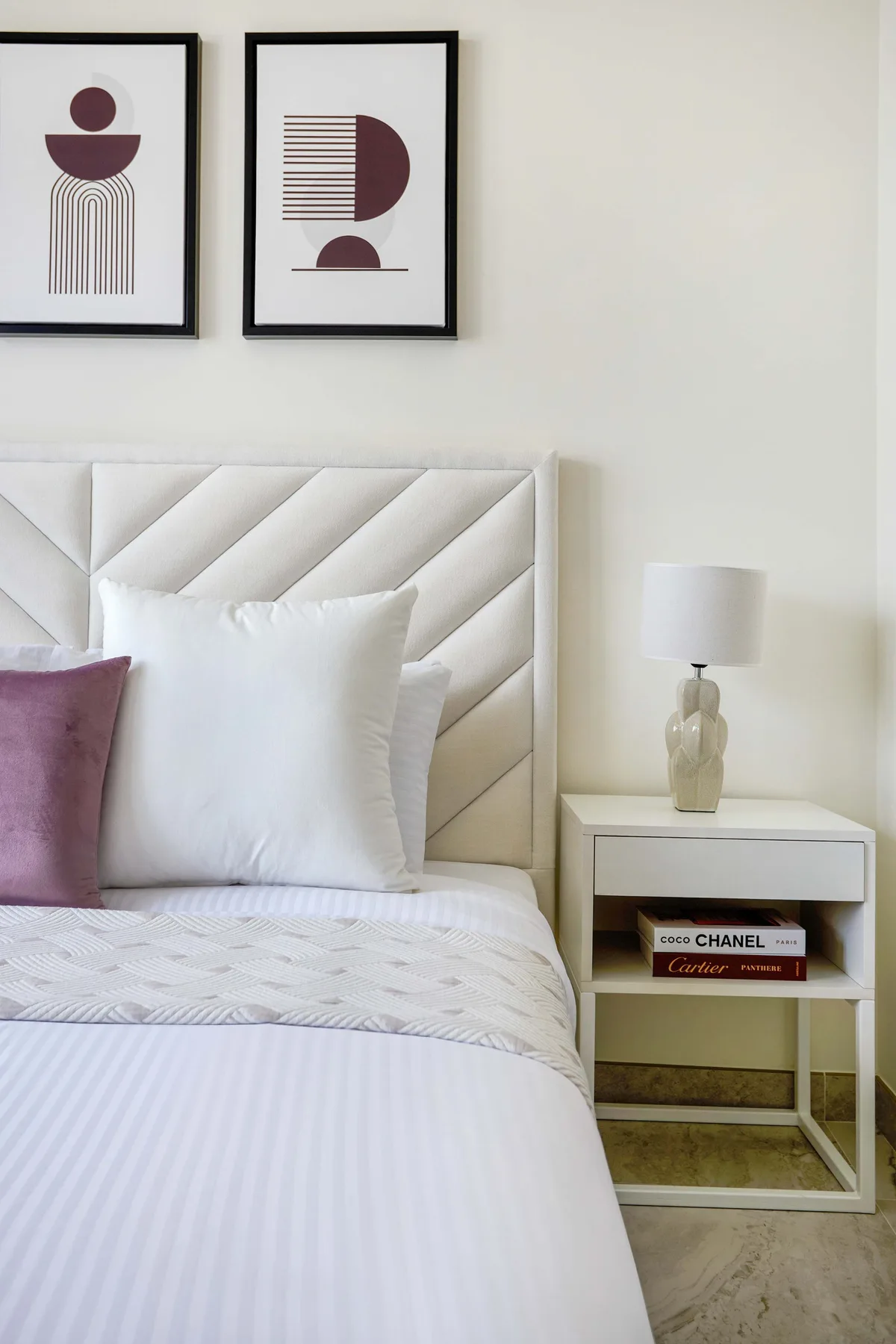 Un dormitorio con una cama ordenada, cuadros enmarcados y una mesita de noche.