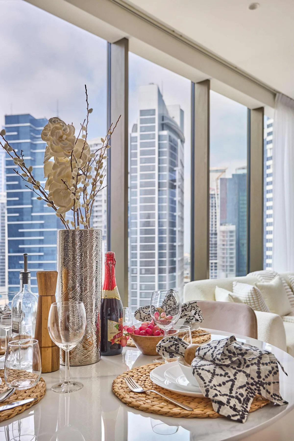 Una mesa de comedor junto a grandes ventanales con vistas a edificios de la ciudad.