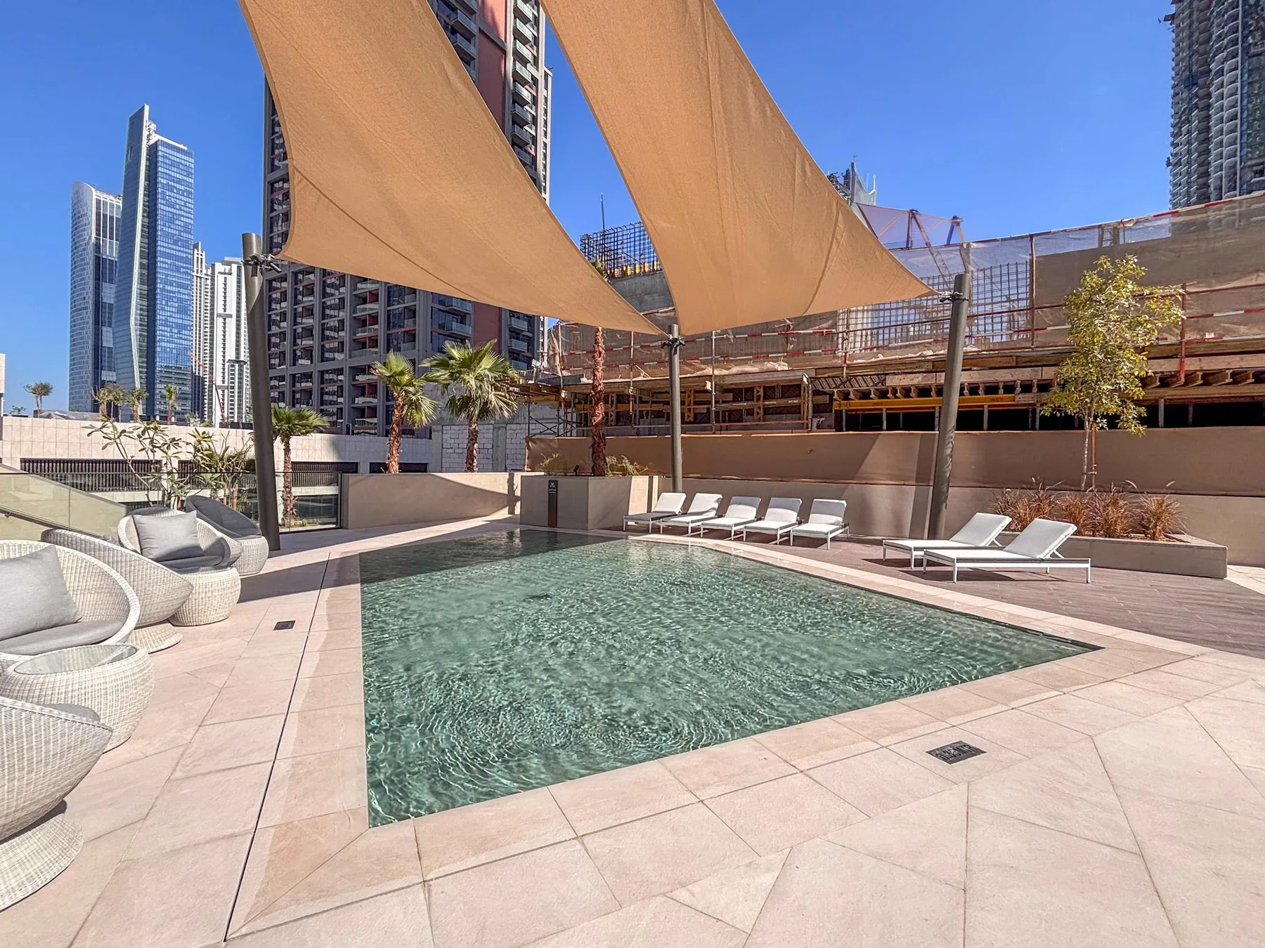 Una piscina al aire libre con tumbonas y toldos, rodeada de edificios urbanos.