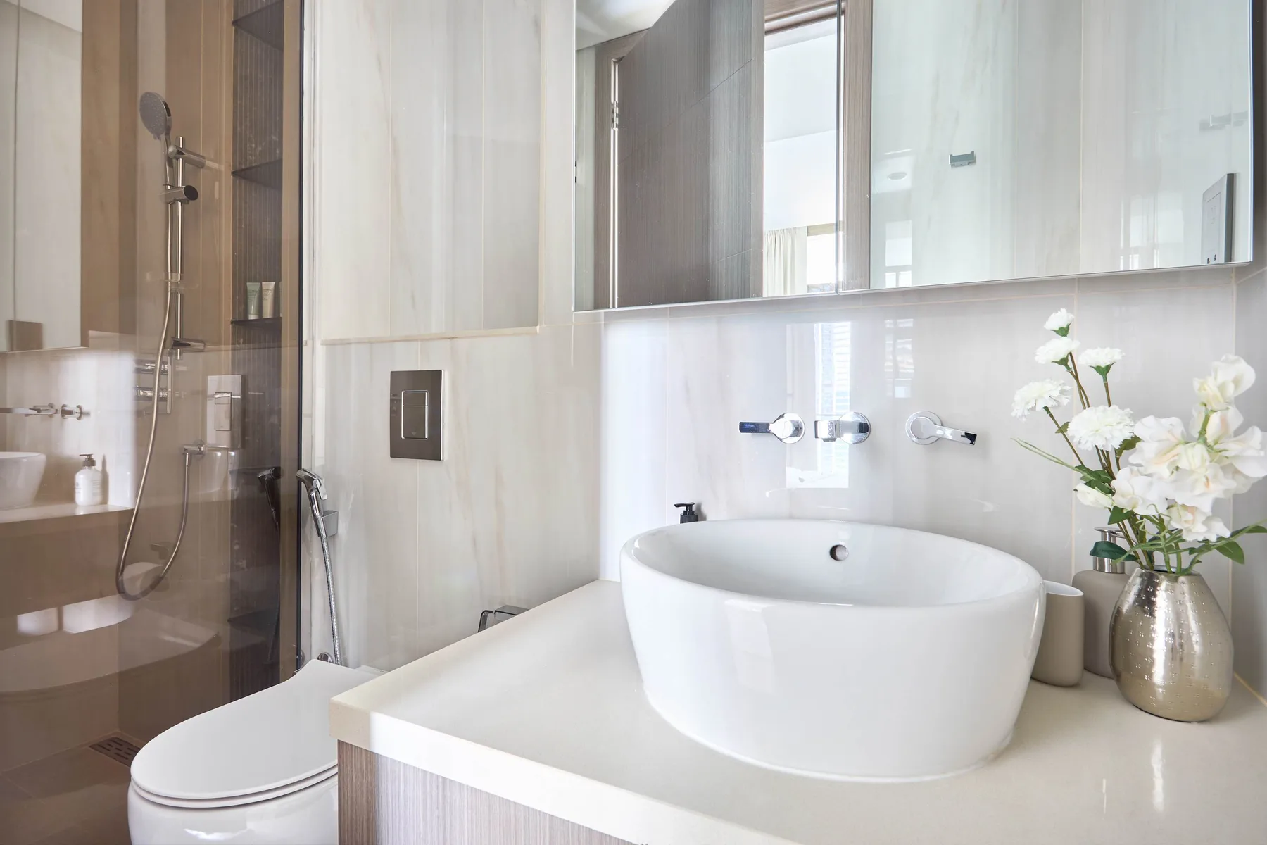 Un baño luminoso con lavabo sobre encimera, espejo de pared y ducha de vidrio.