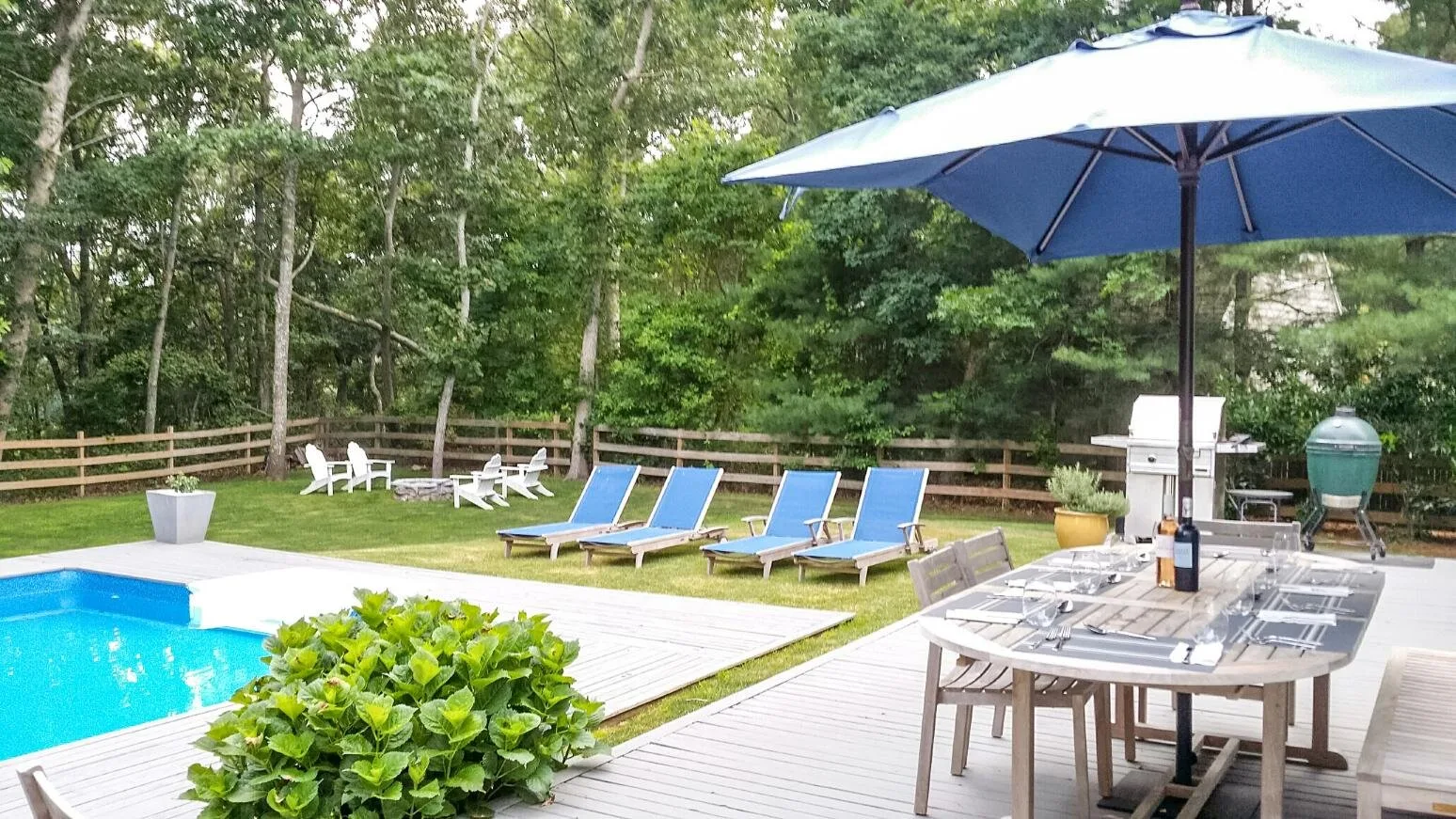 Una terraza junto a la piscina con asientos reclinables y una mesa bajo una sombrilla.