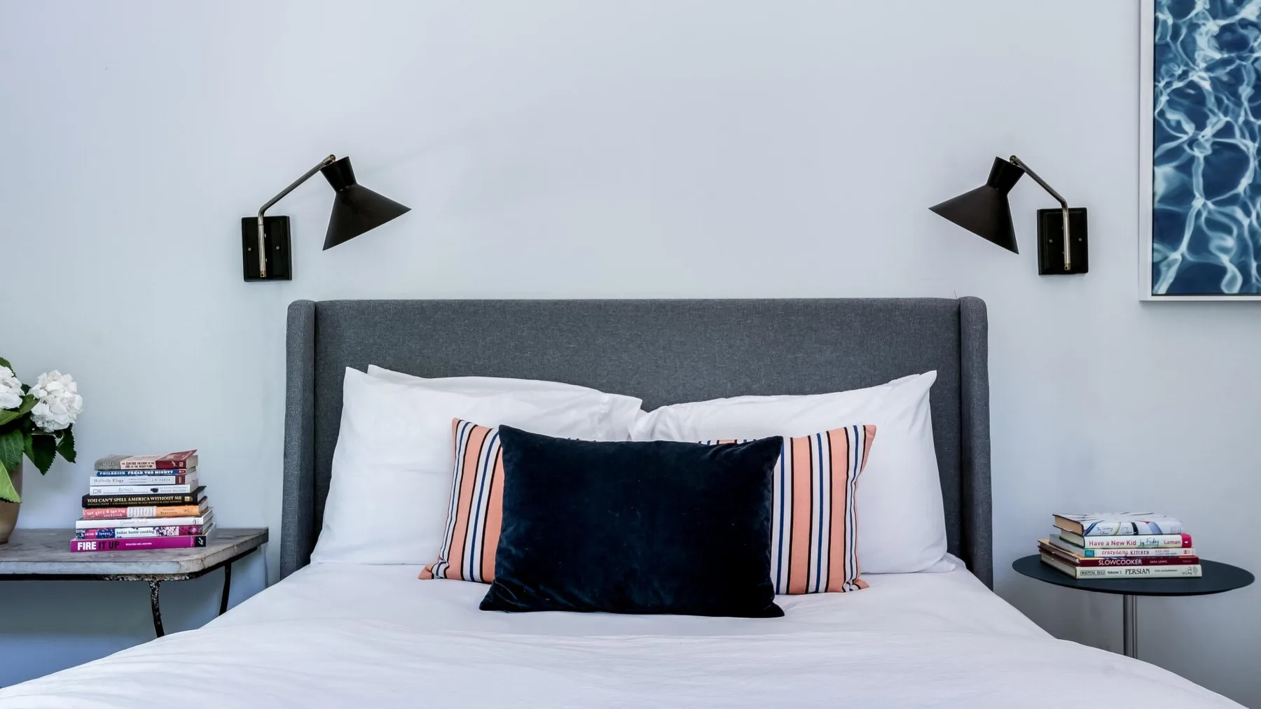 Una cama bien tendida con varias almohadas está debajo de dos lámparas de pared.