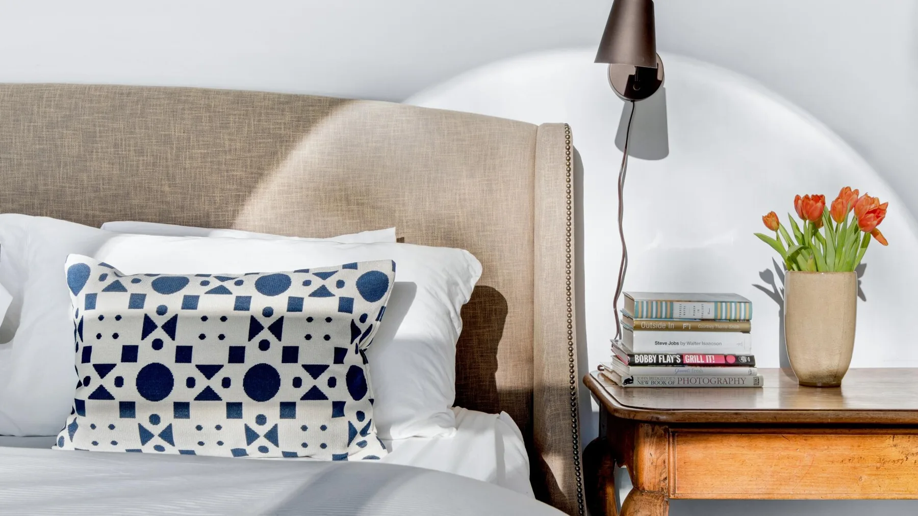 Dormitorio con una cama, cojines estampados y una mesa de noche de madera.