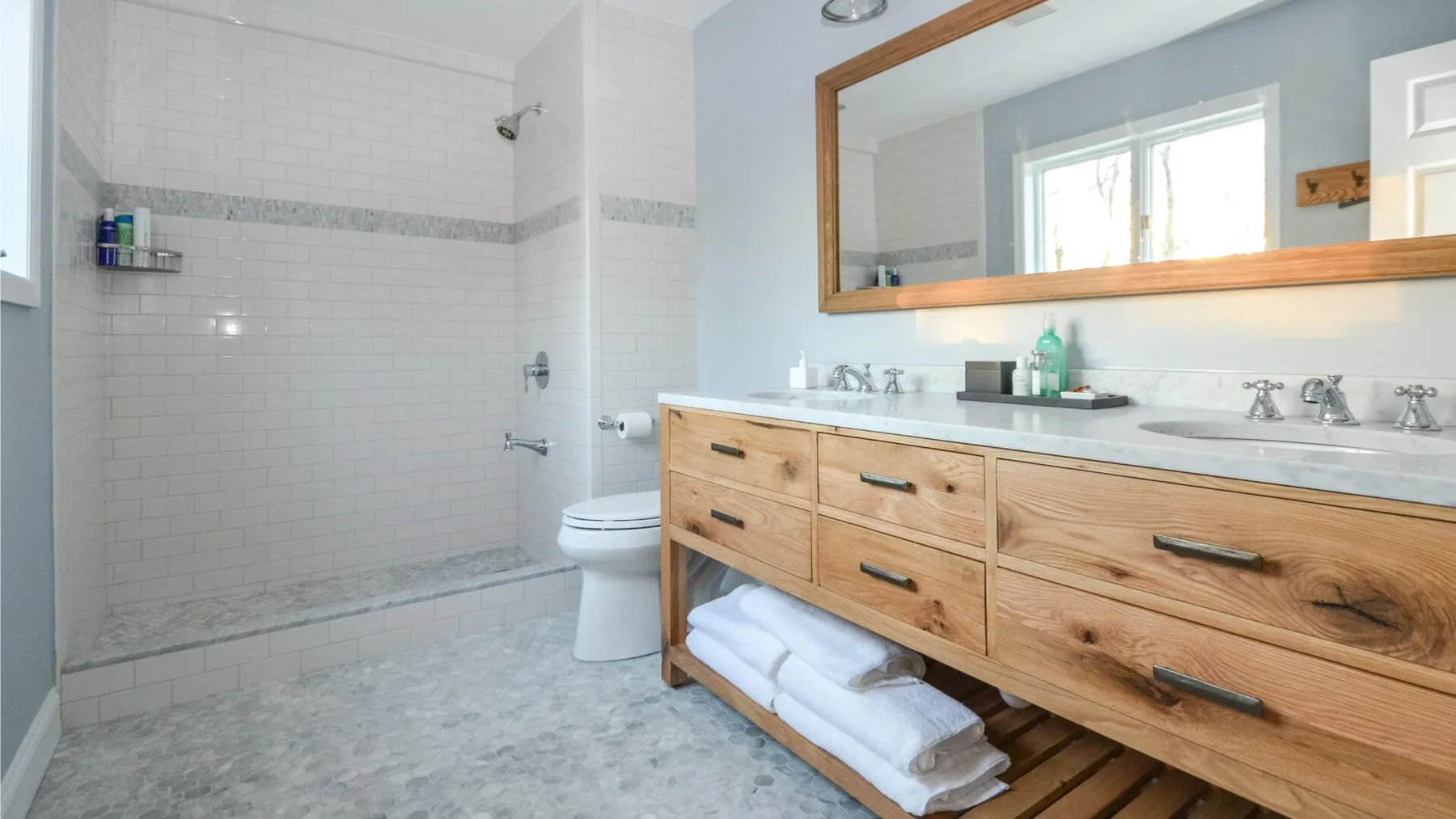Un baño luminoso cuenta con una ducha alicatada, un inodoro y un largo tocador de madera.