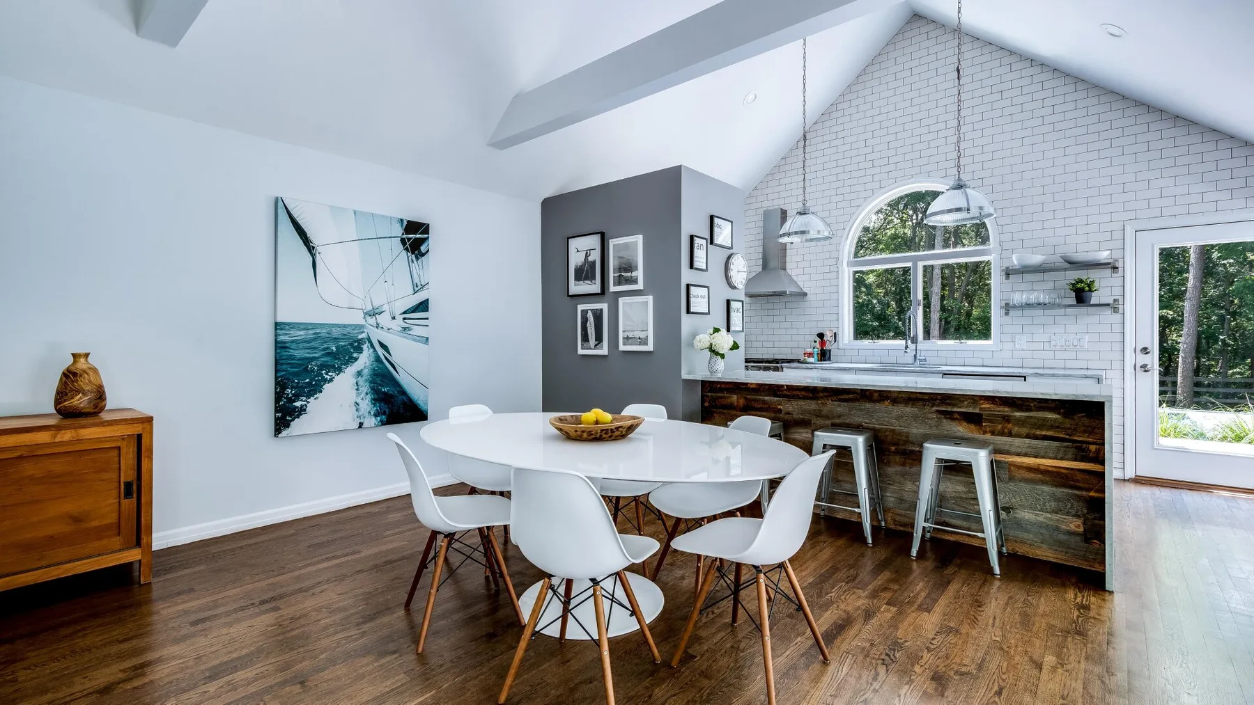 Un comedor luminoso con una mesa blanca junto a una isla de cocina y ventanas grandes.