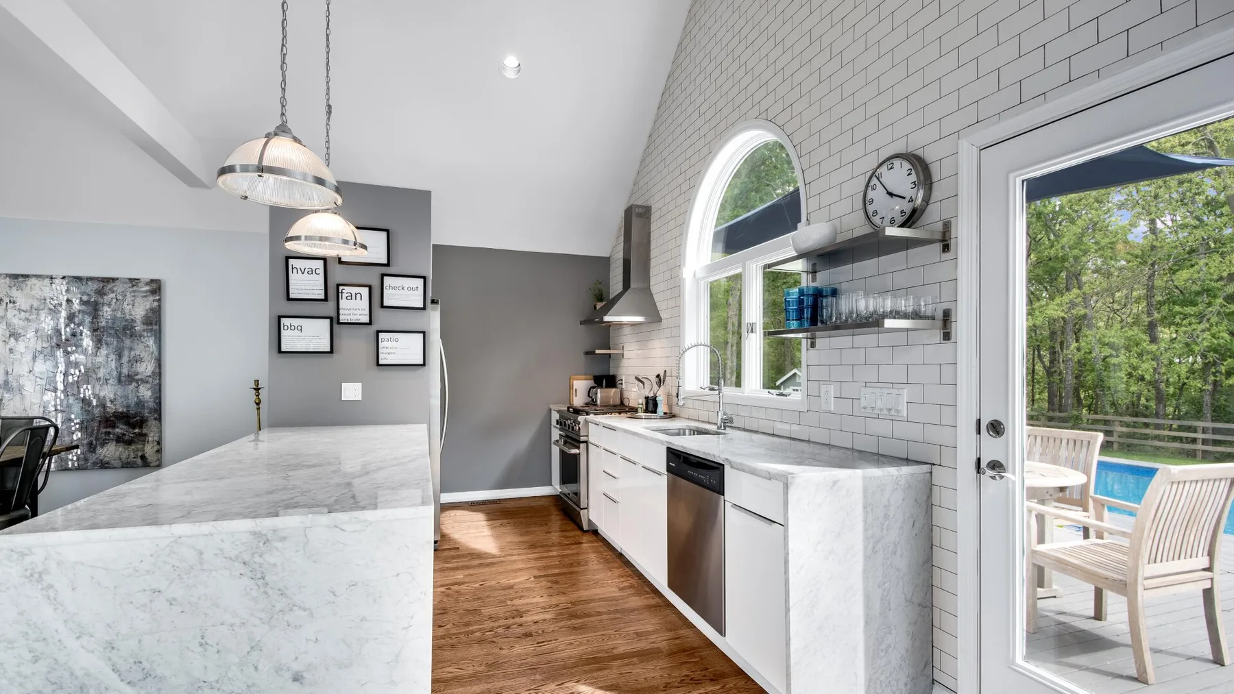 Una cocina luminosa con una isla larga, gabinetes blancos y una puerta de vidrio que da a un patio.