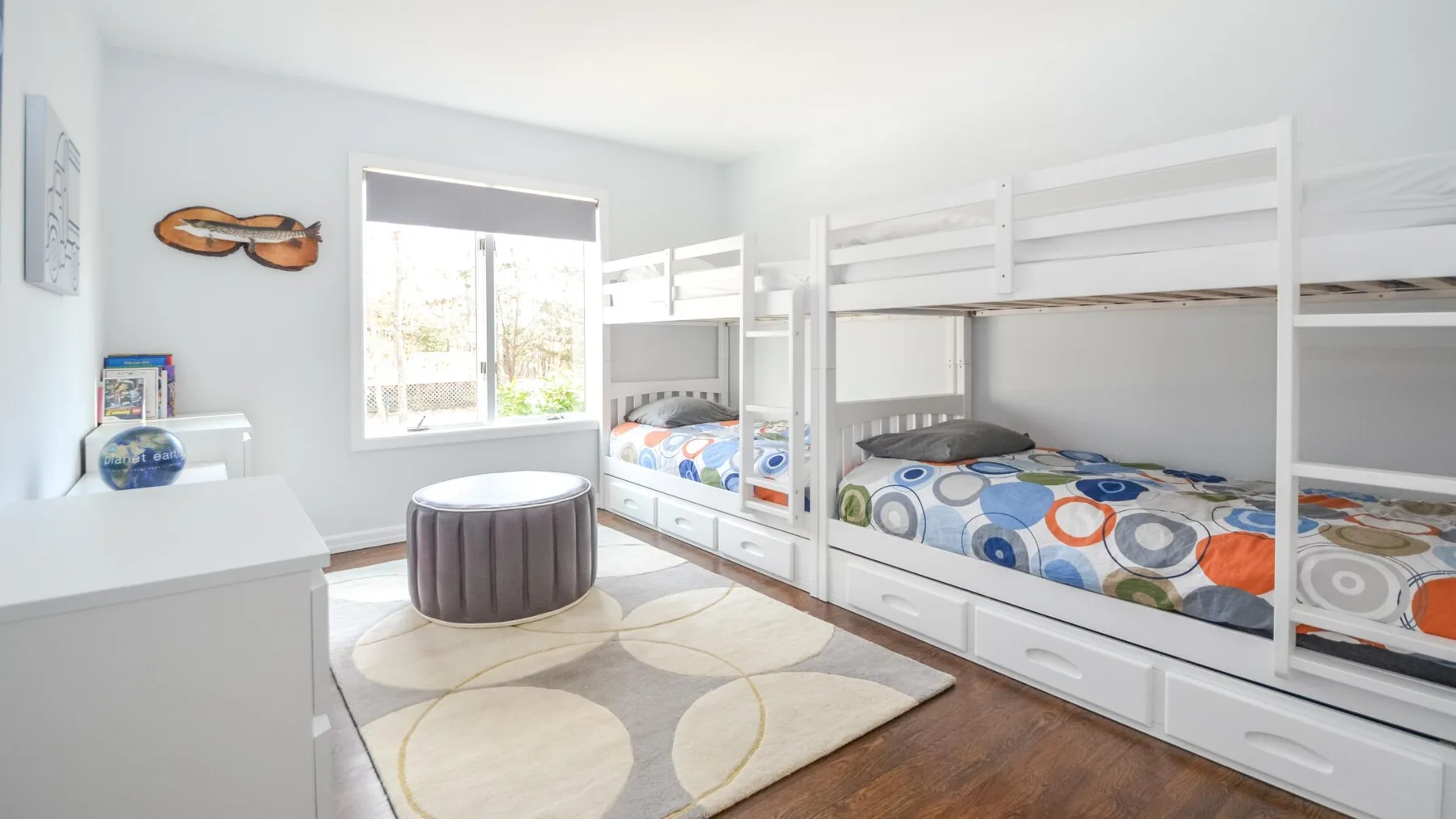 Un dormitorio luminoso con literas blancas y ropa de cama estampada y colorida.