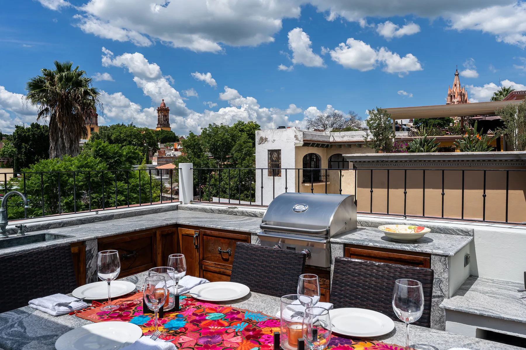 A rooftop dining area with a set table, outdoor kitchen, and city views.