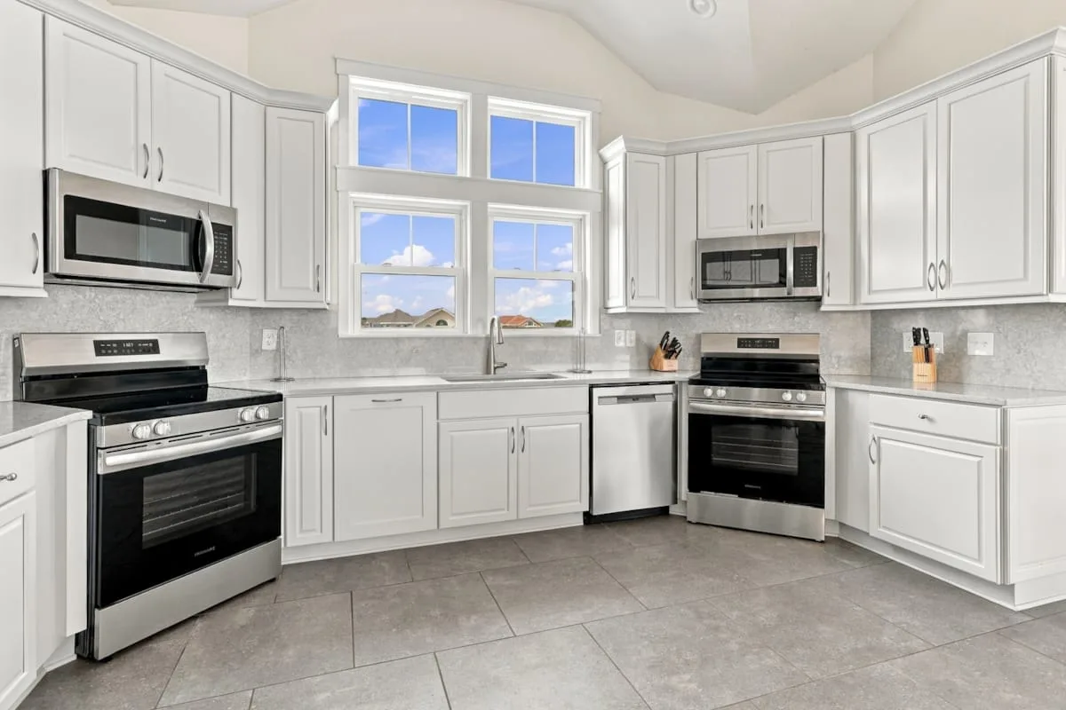 Una cocina luminosa con gabinetes blancos, dos estufas y una ventana sobre el fregadero.