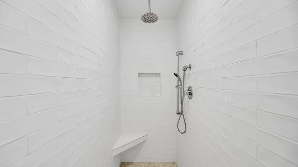 A white-tiled shower area with a wall-mounted shower fixture and a built-in bench.
