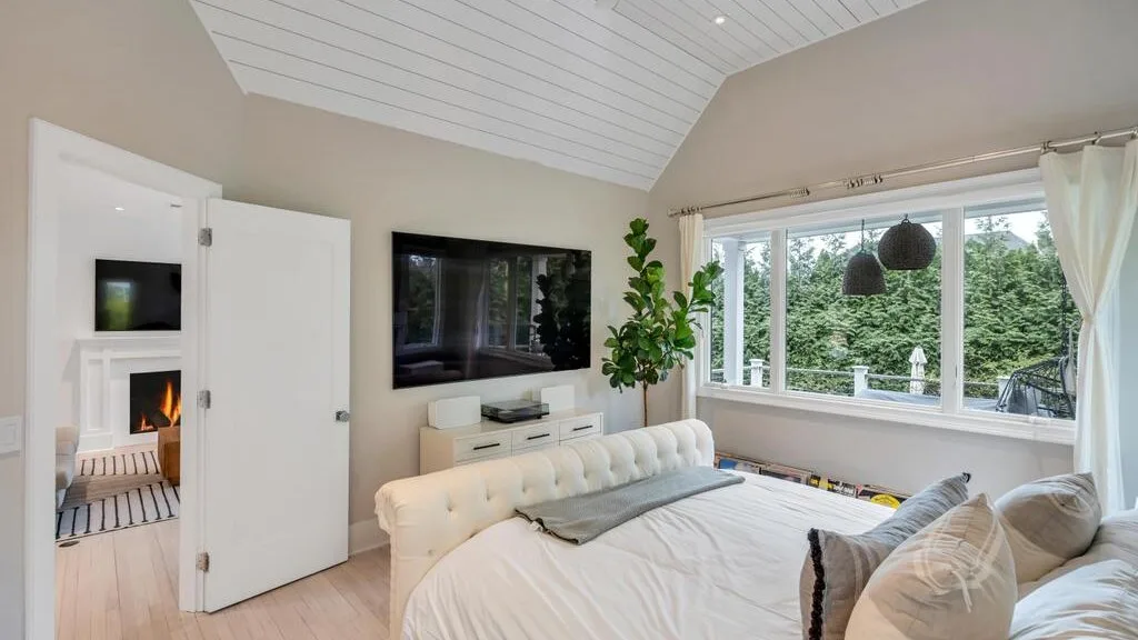 A bright bedroom with a bed beside wide windows overlooking greenery.