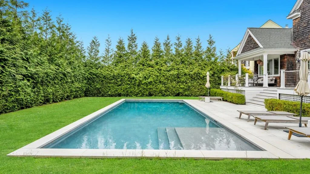 An outdoor swimming pool beside a green lawn and a house.