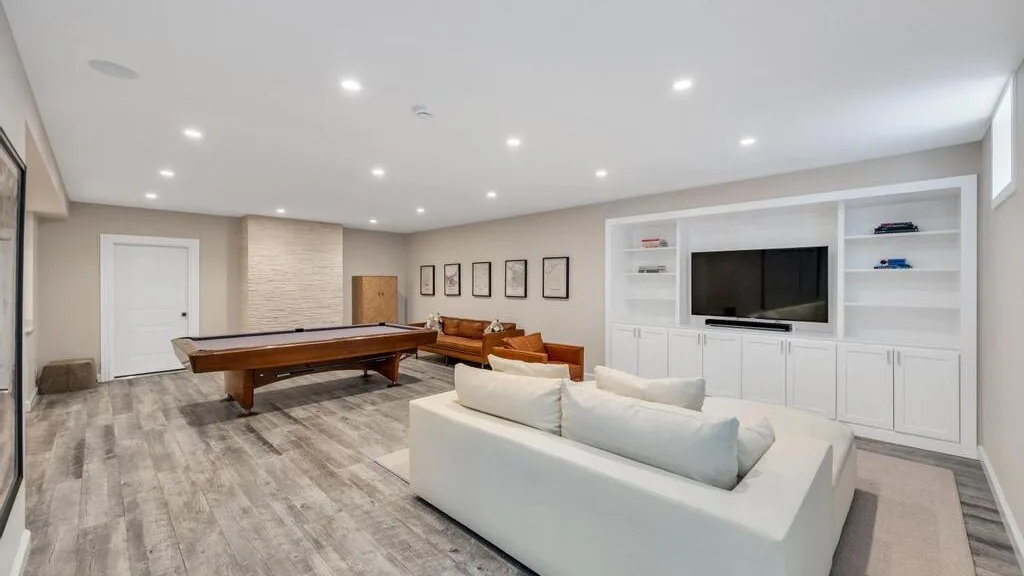 A bright recreation room features a pool table, seating, and built-in cabinets.