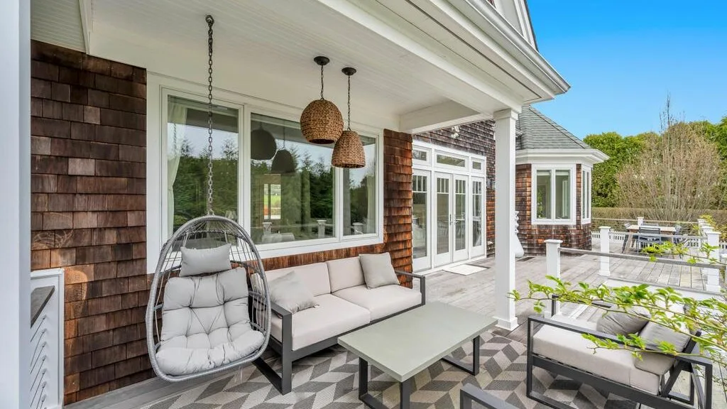 An outdoor patio with seating, a hanging chair, and large windows.