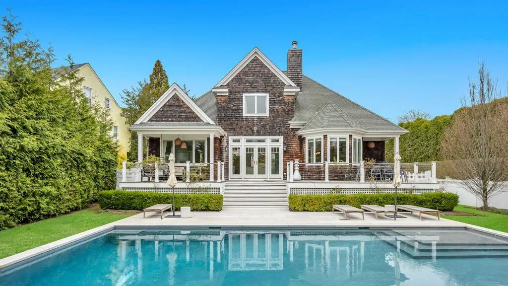 A large house with a white terrace overlooks a swimming pool.