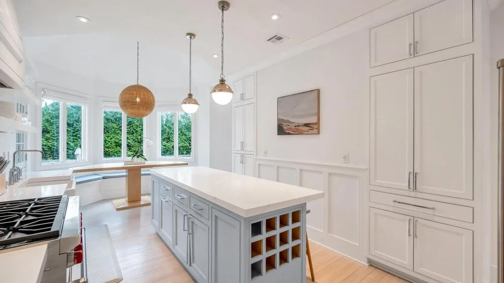 A bright white kitchen with a central island and large windows.