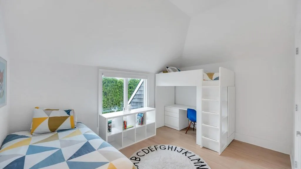 A bright bedroom with a bed beside a desk and open shelving.