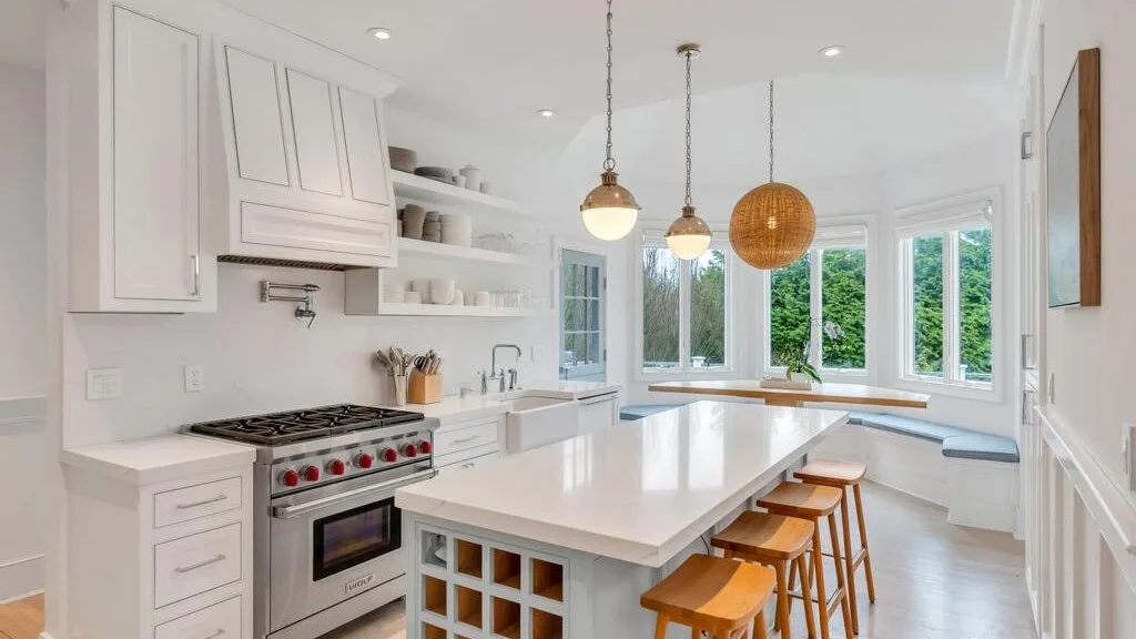 A bright white kitchen with a large island and windows overlooking greenery.